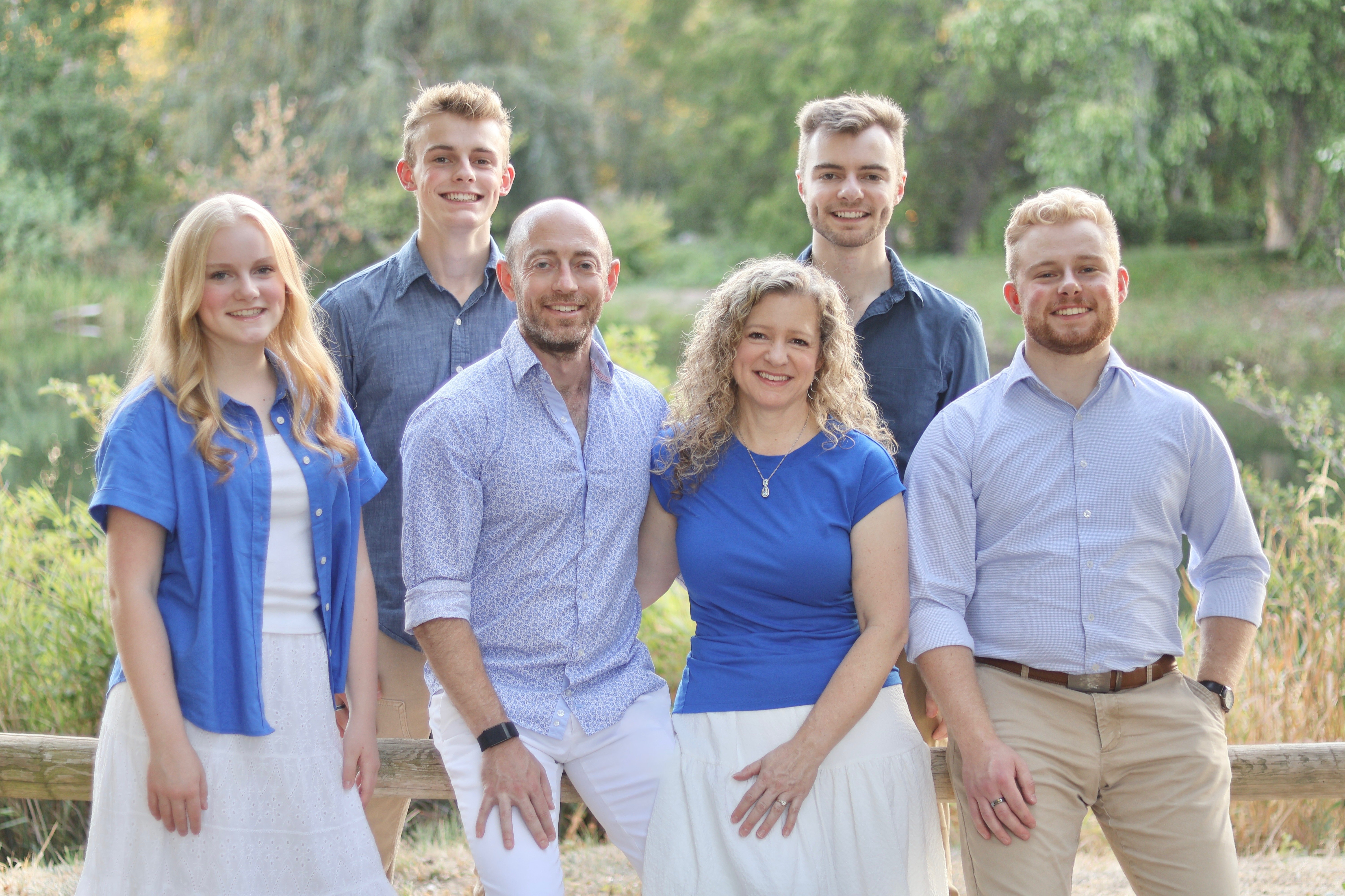 The Hymas family standing together outdoors beside a wooden fence